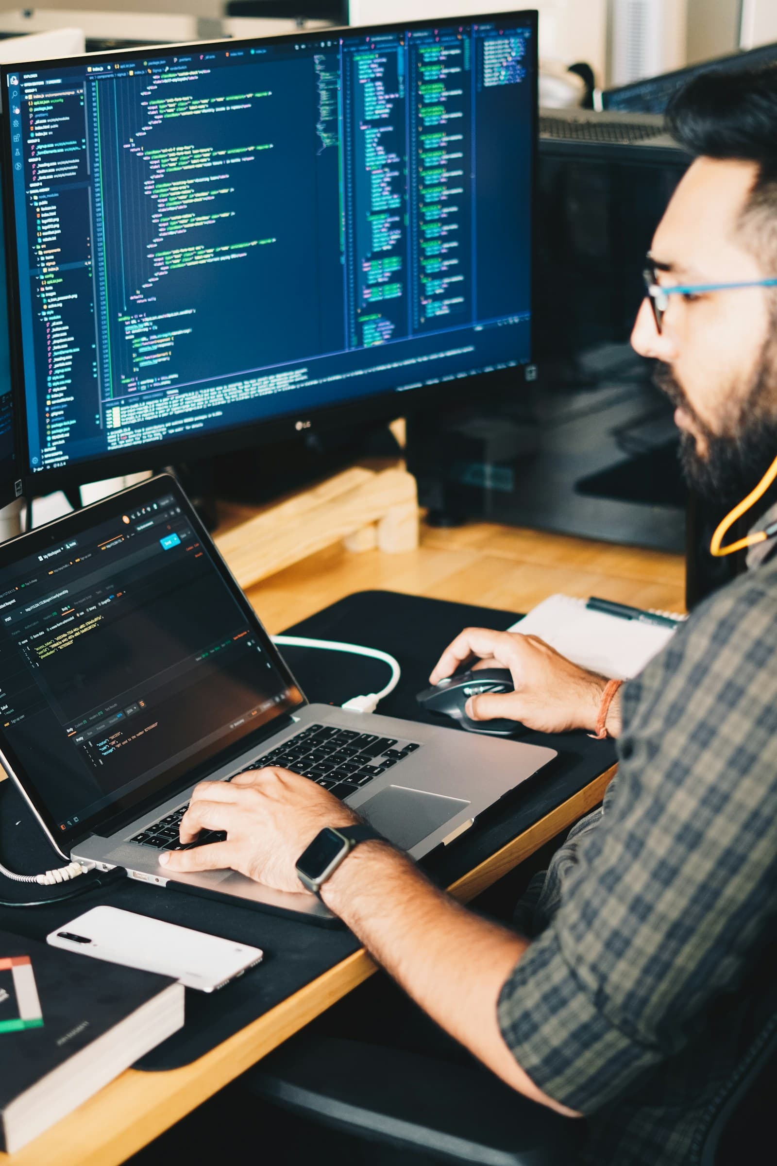 A developer working on a laptop connected to a monitor showing code