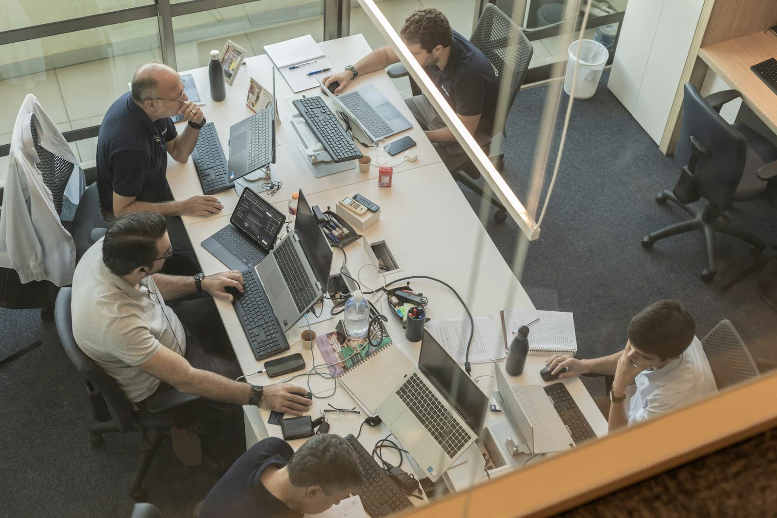 An overhead view of a team working at laptops in a glass-walled office