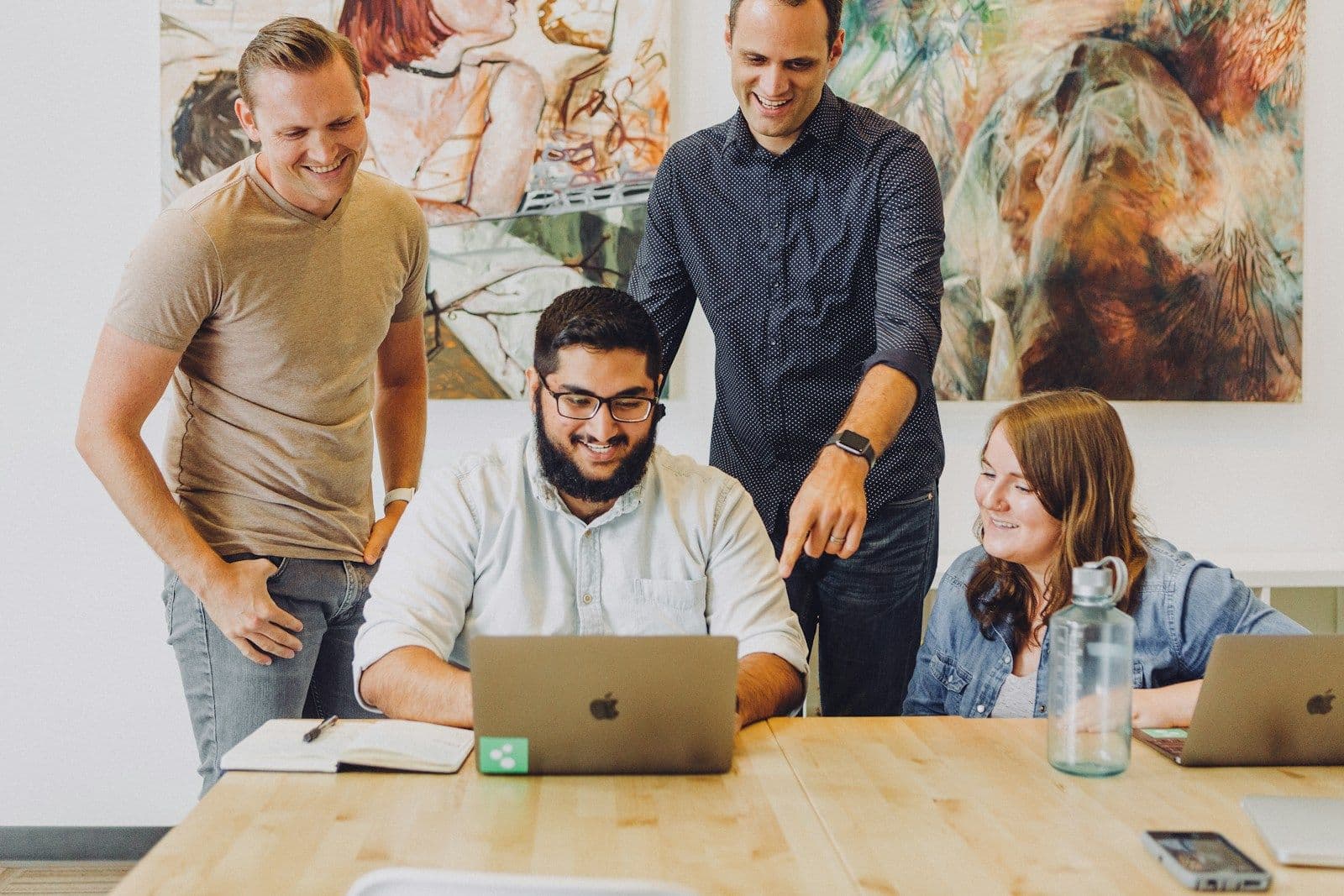 Four colleagues smiling as they work together around a laptop