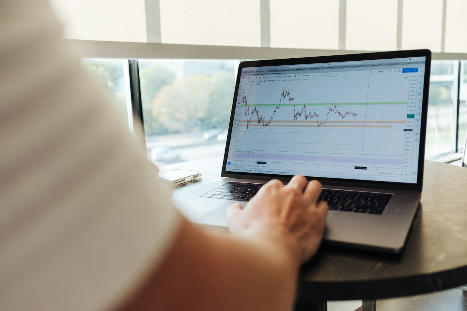 A person reviewing a price chart on a laptop beside a window