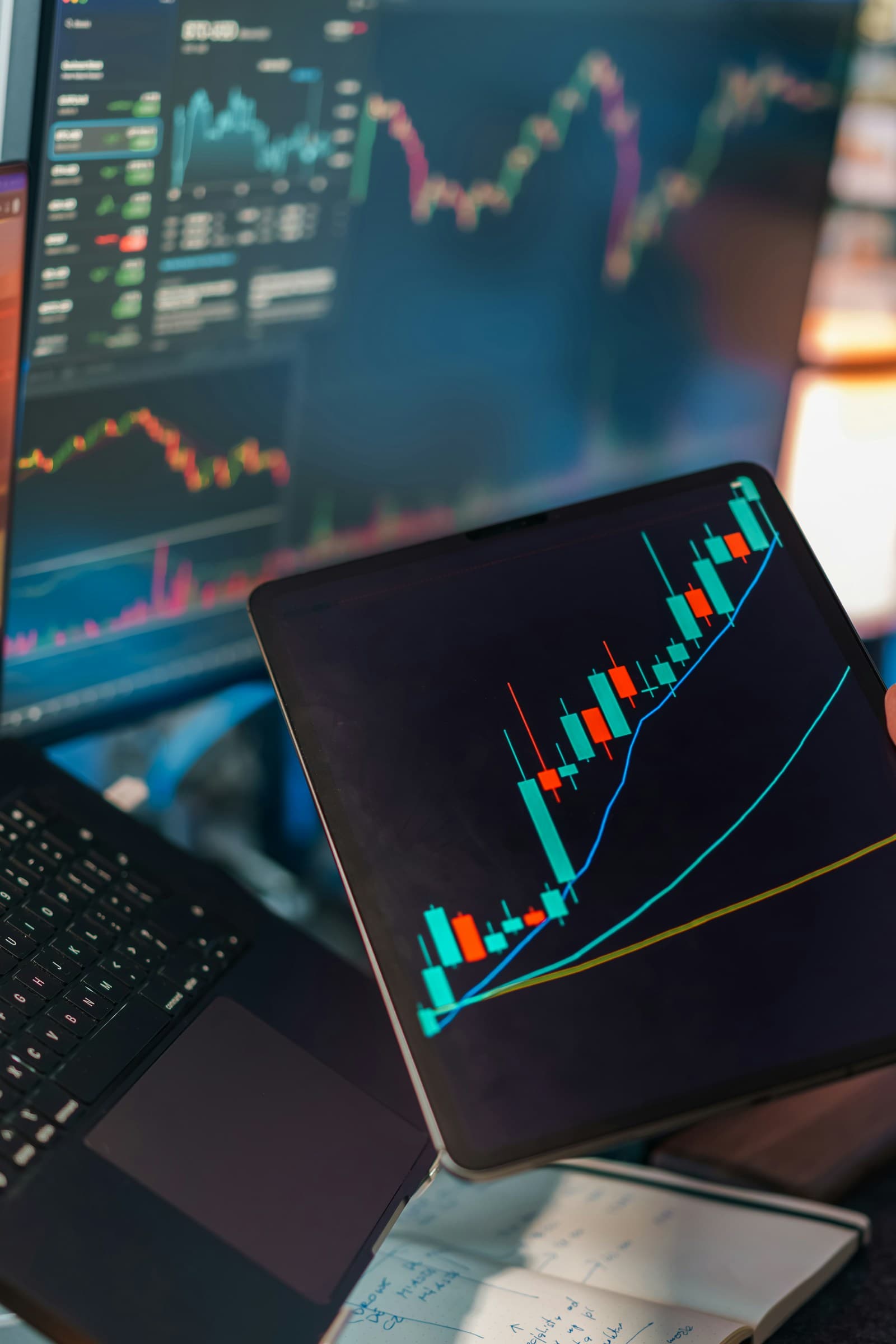 Trading charts displayed across several screens and a tablet