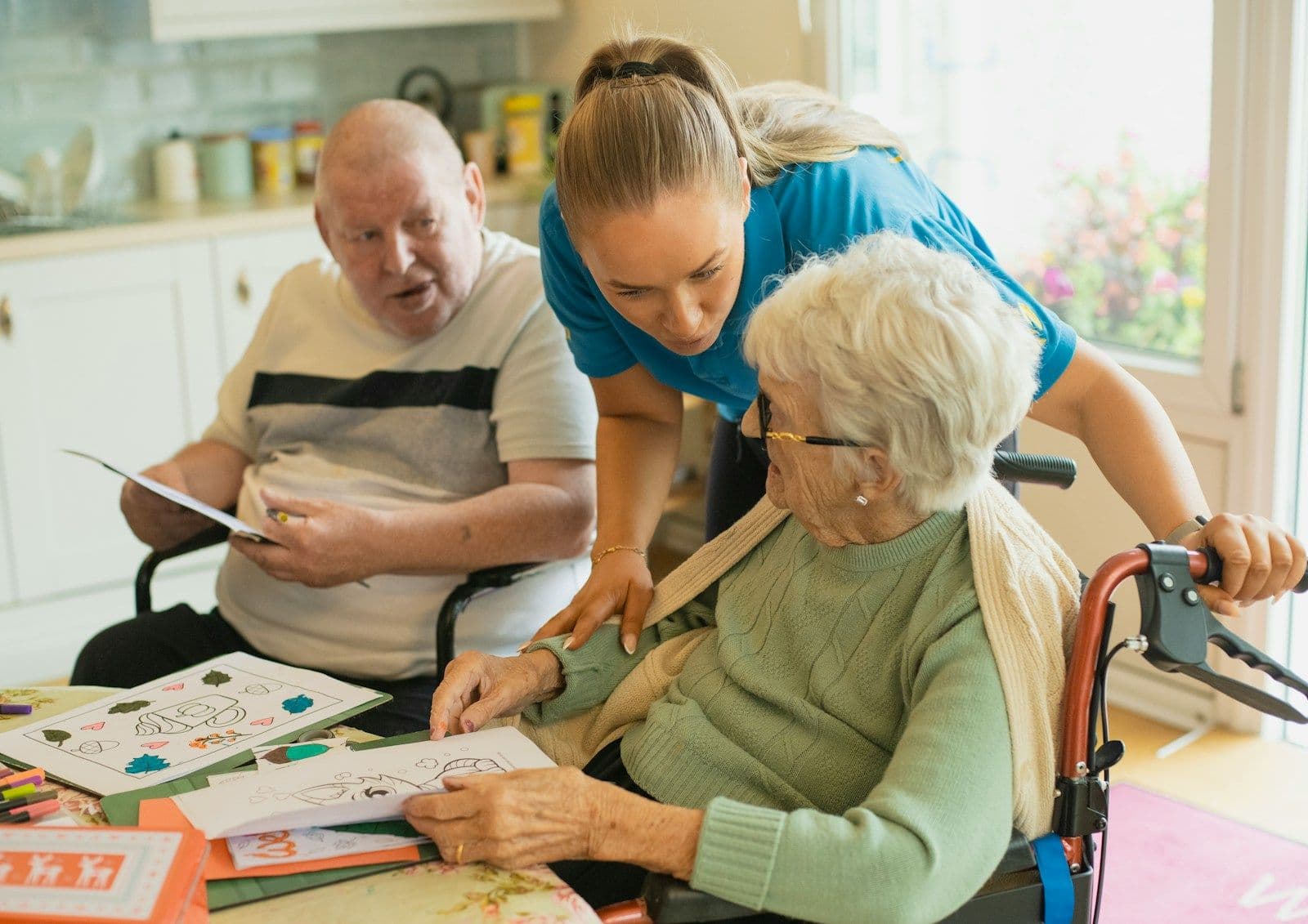 A care worker helping two older residents with an activity at a table in a care home