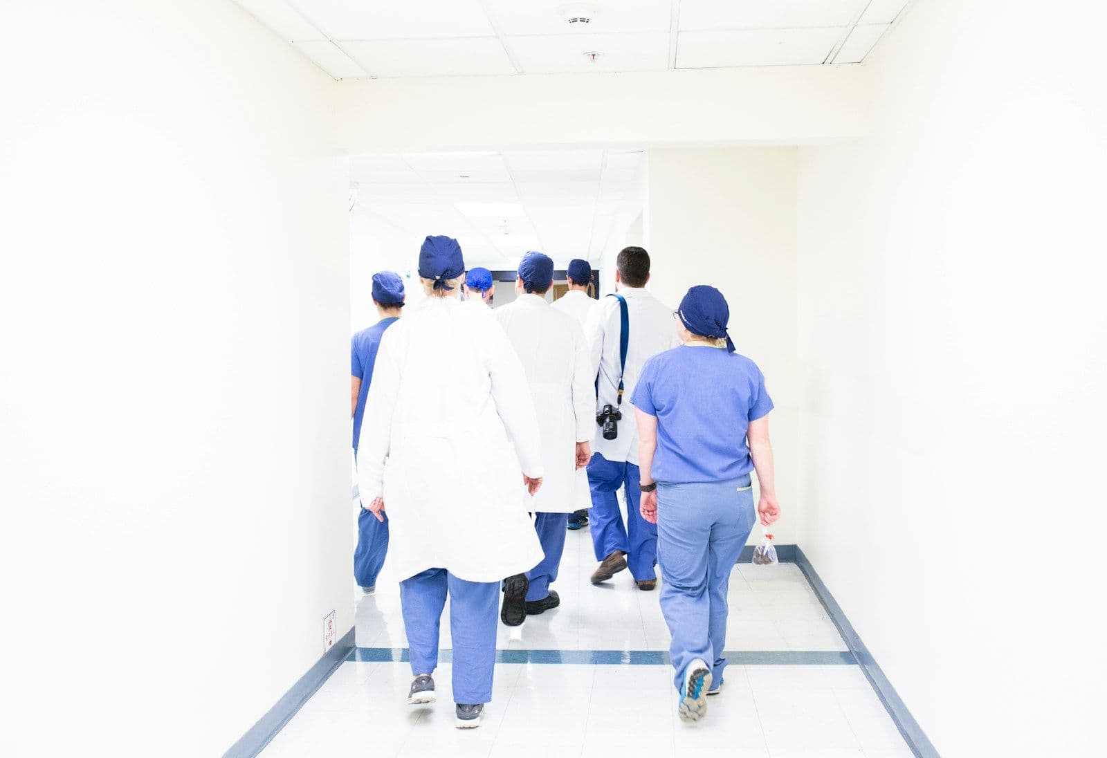 A team of clinicians in scrubs and white coats walking down a bright hospital corridor