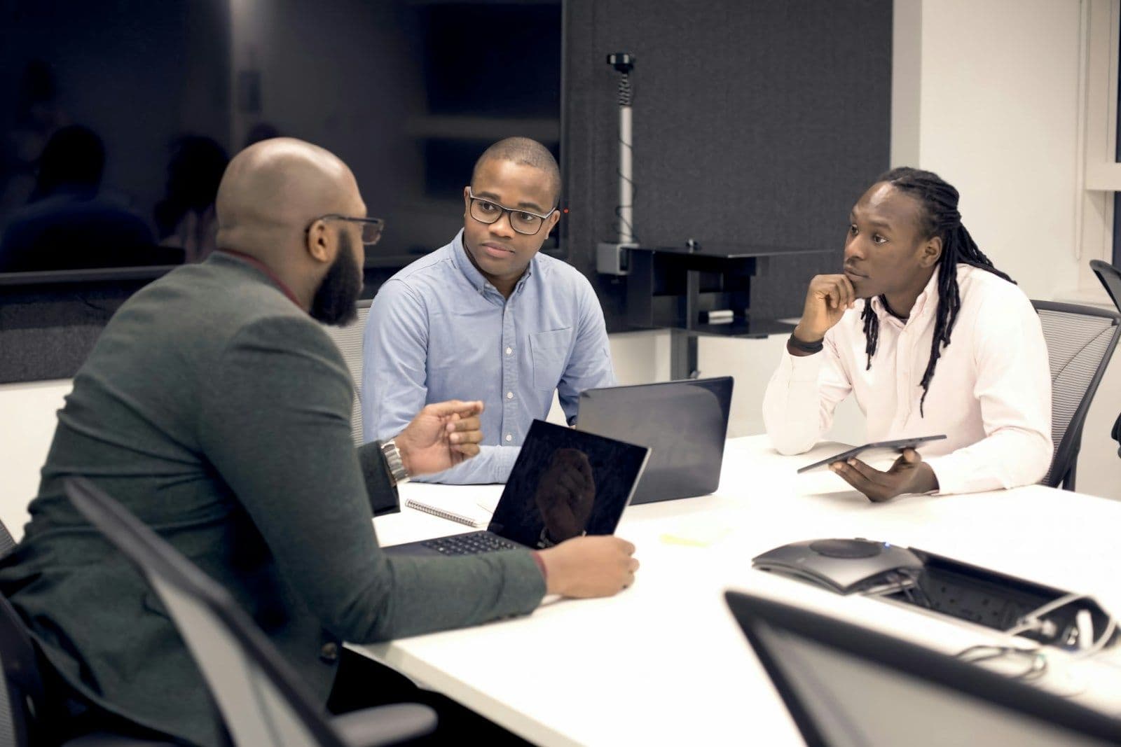 Three colleagues discussing a project around a table with laptops and a tablet
