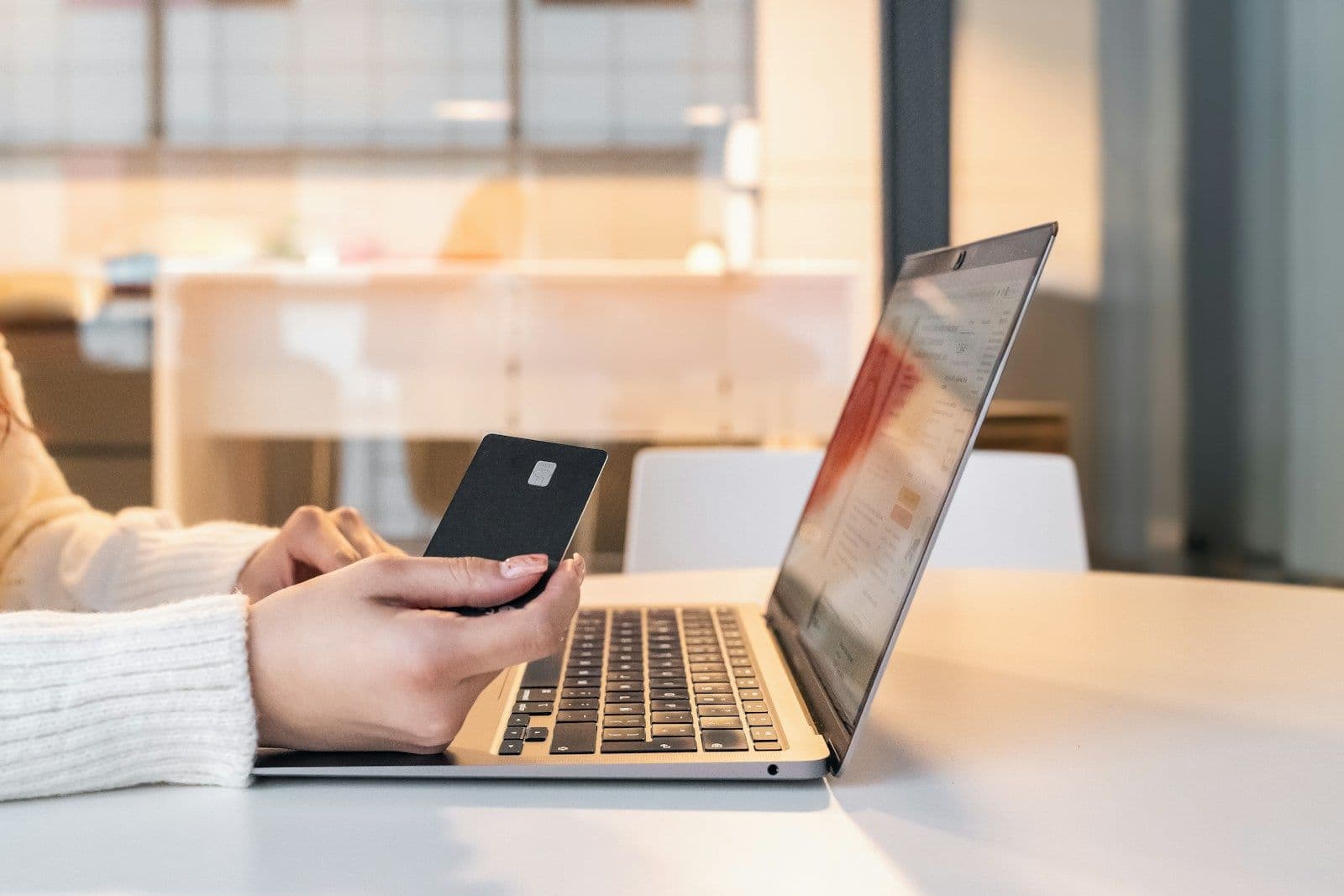 A person holding a payment card while shopping online on a laptop