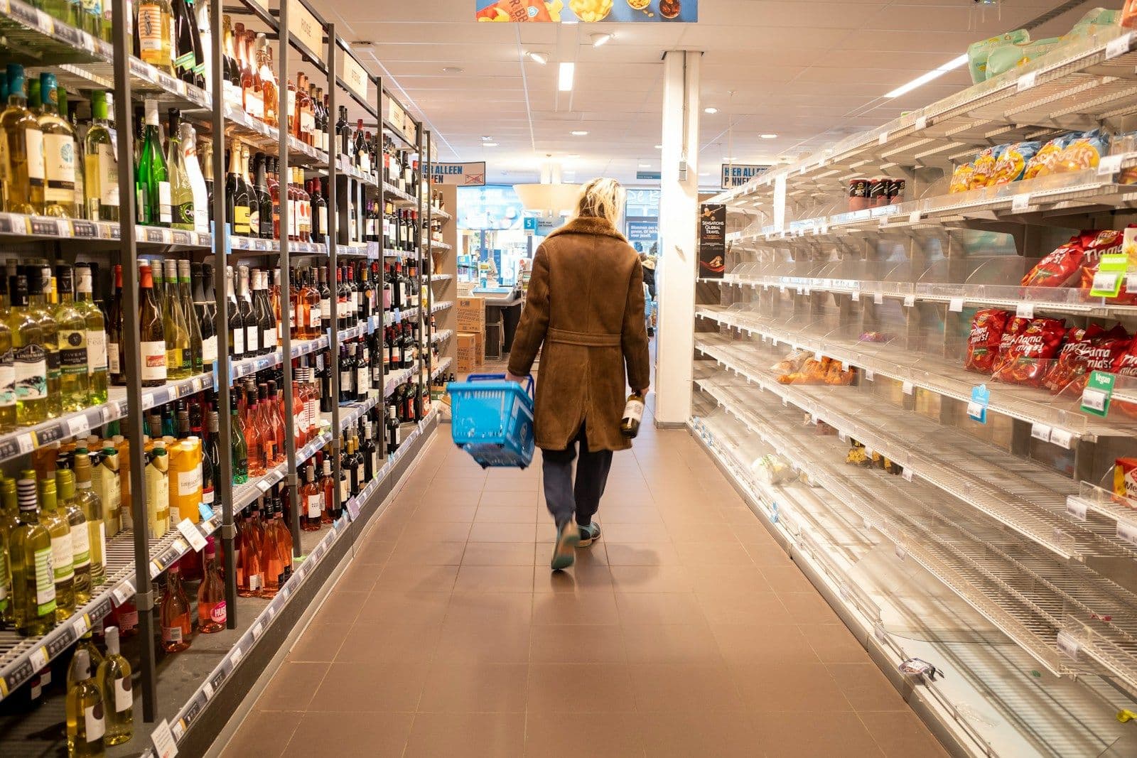A shopper carrying a basket down a supermarket aisle
